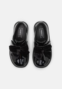 Schwarze lacklederne Schuhe mit einer runden Zehenform, die vorne eine große schwarze Samt-Schleife sowie eine strukturierte Gummisohle aufweisen.