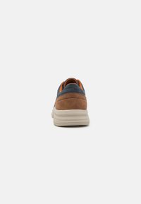 Baskets pour hommes avec un talon et des côtés en daim marron, une tige bleu foncé, des accents orange et une semelle beige ; conçues pour le confort et le soutien.