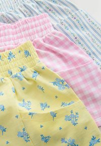 Tre paia di pantaloncini da pigiama: gialli con stampa floreale blu, a quadretti rosa e bianchi con righe blu e piccoli dettagli floreali.