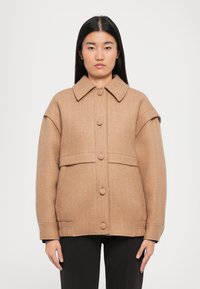 Barna gyapjúkeverék dzseki gallérral, nagy gombokkal, két elülső zsebbel, oversize ujjal és strukturált dizájnnal, fekete nadrággal párosítva.