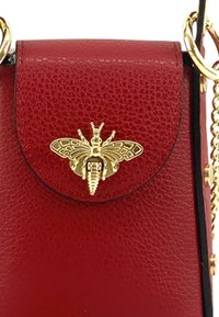 Rode leren handtas met een gouden bij-vormige sluiting. Heeft een klepopening en een metalen kettingband. Compact ontwerp.