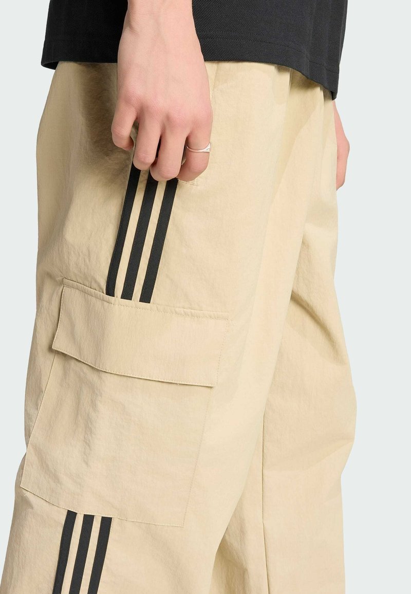 Beige Cargohose mit schwarzen Seitenstreifen und großer Seitentasche. Der Stoff wirkt leicht und hat eine leicht geknitterte Textur.