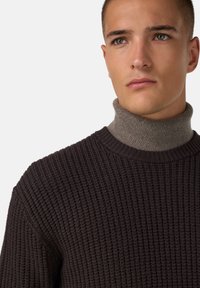 Pull à côtes marron foncé associé à un col haut gris clair. Il présente un tissu texturé et un col rond classique.