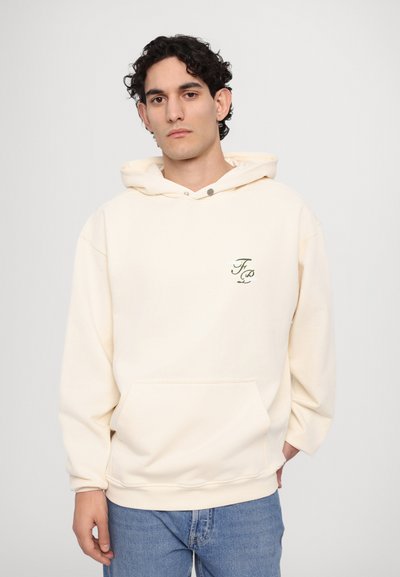 Cream hoodie made of soft fabric, featuring a front pocket, a drawstring hood, and small green embroidered logo on the chest.
