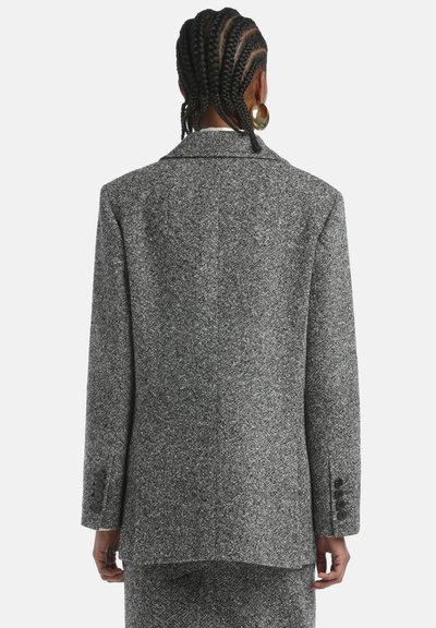 Szary żakiet w wzór houndstooth o strukturalnym kroju, z klapami typu notch i mankietami z trzema guzikami. Materiał ma teksturowaną, tkana powierzchnię.