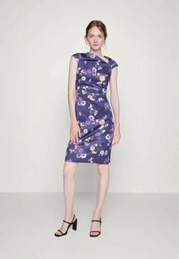 Vestido floral roxo em satin com um design justo, mangas curtas e um comprimento até ao joelho. Sandaļas pretas de tiras completam o visual.