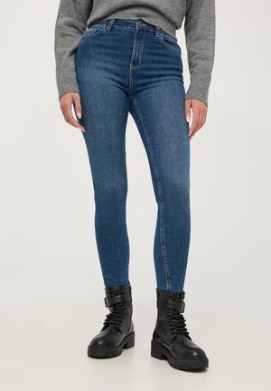 Slim-fit, wysokogatunkowe, niebieskie dżinsy z wysokim stanem, wykonane z denimu z minimalnym blaknięciem, w połączeniu z czarnymi sznurowanymi butami wojskowymi z grubą podeszwą.
