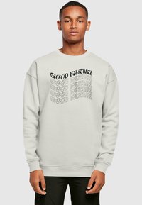 Helles graues Sweatshirt mit Rundhalsausschnitt, auf der Vorderseite mit schwarzem Text "GOOD KARMA" in verschiedenen Stilrichtungen und Ausrichtungen versehen. Weicher Stoff.