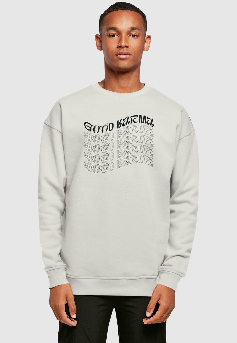 Helles graues Sweatshirt mit Rundhalsausschnitt, auf der Vorderseite mit schwarzem Text "GOOD KARMA" in verschiedenen Stilrichtungen und Ausrichtungen versehen. Weicher Stoff.