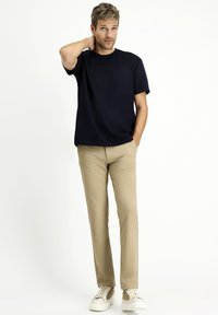 T-shirt blu navy a maniche corte, abbinata a pantaloni beige e sneakers bianche. L'outfit presenta una vestibilità ampia e un design minimalista.