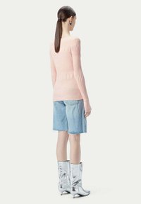 Ljusrosa ribbad stickad tröja, blå denimshorts och glänsande silverfärgade knähöga stövlar, sedd bakifrån. Släta texturer och åtsittande design.