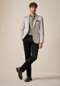 Hellgrauer Blazer, gemustertes Hemd, schwarze Cordhosen und schwarze Schuhe. Verfügt über ein Einstecktuch und strukturierte Knöpfe. Slim-Fit-Design.