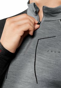 Pullover grigio con zip e colletto alto, caratterizzato da accenti neri e tessuto texturizzato. Logo "FALK" vicino alla cerniera, mano che afferra il tirante della cerniera.