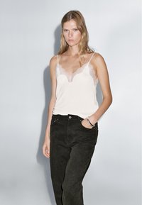 Lace-trimmed cream tank top with thin straps, paired with high-waisted black jeans. Features a slim fit and smooth fabric texture.