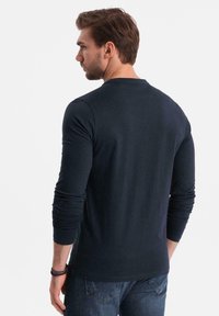 T-shirt a maniche lunghe blu navy in un materiale morbido, con scollatura a girocollo e design aderente, con polsini arrotolati e una texture liscia indossato da un modello.