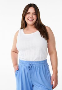 Top blanco de tirantes acanalados con patrones texturizados verticales, combinado con pantalones de tiro azul claro con cordón. Ambas prendas son sencillas y de estilo casual.