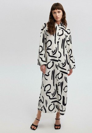 Maxi dress in cream fabric with bold black abstract patterns, featuring a button-up front, long sleeves, and a relaxed fit.