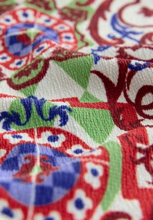 Tissu textile présentant des motifs complexes en rouge, bleu, vert et blanc ; surface texturée avec une apparence tissée douce.