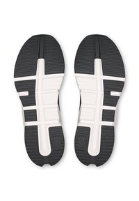 Le suole delle scarpe da ginnastica in gomma presentano un motivo di battistrada nero con accenti bianchi sul sottopiede, progettate per trazione e supporto durante l'attività atletica.