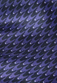 Lilla mønstret stoff med hundetannsdesign i vekslende mørke og lyse nyanser, fremhevet av små hvite trekantede former.