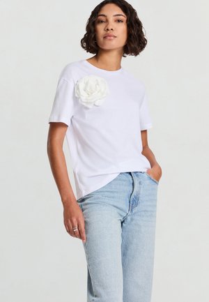 Maglietta bianca in cotone con scollo rotondo e maniche corte, caratterizzata da un grande dettaglio a rosa di tessuto sul petto sinistro e vestibilità comoda.