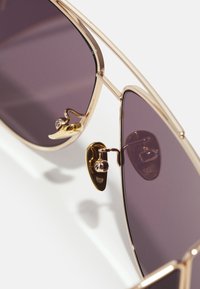 Occhiali da sole aviator in metallo dorato con lenti viola scuro. Presentano un design a doppio ponte e naselli regolabili per una vestibilità sicura.