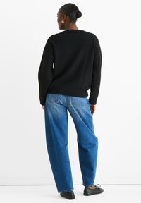 Black knitted sweater with a rounded neckline, paired with loose blue denim jeans. The outfit has a relaxed fit and minimal detailing.