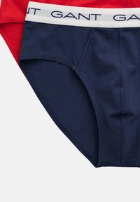 Baumwollunterwäsche in Marineblau und Rot, mit einem weißen Bund, der das Logo "GANT" trägt. Glatte Textur mit einer Nahtdetails an den Nähten.