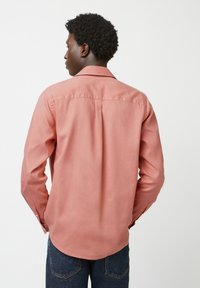 Langarmshirt in zacht, licht koraal stof. Kenmerken een klassieke kraag, plooien aan de achterzijde voor gemak, en een gebogen zoom. Gecombineerd met donkere denim.