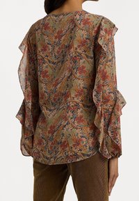 Blus med blommönster och volangärmar, som har jordnära toner av grönt, rött och blått på lättviktig tyg.