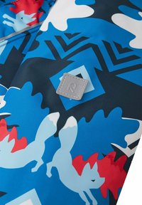 Kleurige stof met blauwe, rode en witte patronen van vossen en abstracte vormen. Bevat een grijze vierkante tag met een reliëf van "R."