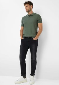 Grünes Baumwoll-Polohemd mit kurzen Ärmeln, kombiniert mit dunklen Slim-Fit-Jeans und weißen Turnschuhen. Einfaches Design, keine sichtbaren Muster oder Logos.