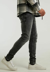 Gray slim-fit jeans with a slight distressed texture, paired with white sneakers. The outfit is accentuated by a black and white plaid shirt.