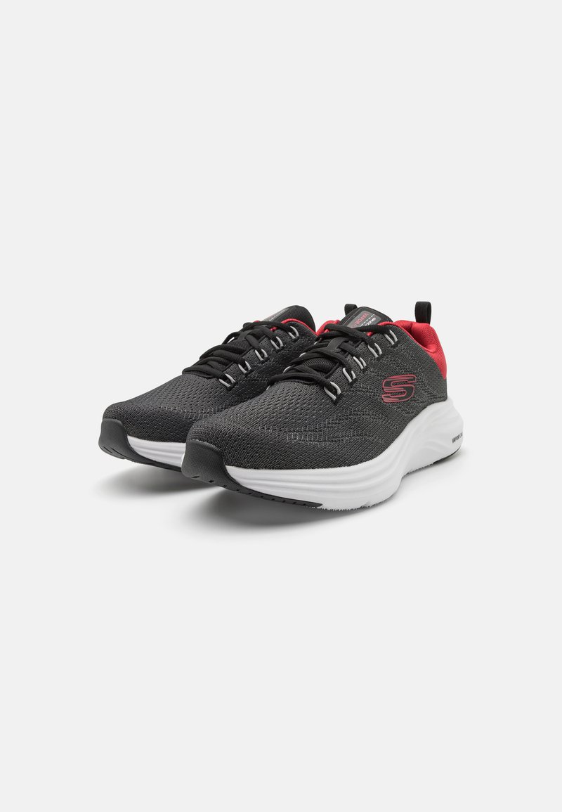 Zapatillas deportivas negras con parte superior texturizada, acentos rojos, entresuela blanca y puntera reforzada. Diseño con cordones y detalle del logo.