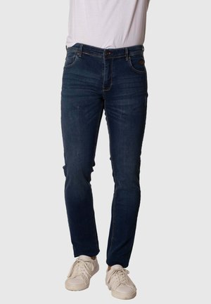 Vaqueros de mezclilla azul oscuro con un diseño ajustado, estilo de cinco bolsillos y costuras en contraste, combinados con zapatillas de color claro.