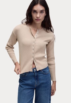 Beige gerippter Cardigan mit Henley-Ausschnitt, Knopfverschluss vorne und langen Ärmeln, kombiniert mit lockeren blauen Jeans.