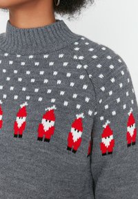 Maglione grigio lavorato a maglia con pois bianchi e una fila di piccoli figures di Babbo Natale rossi e bianchi lungo il petto e le spalle.