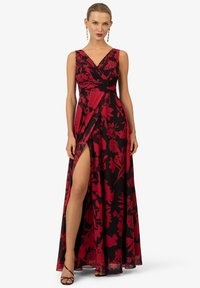 Schwarzes Maxikleid mit rot floralem Muster, V-Ausschnitt, ärmelloses Design und seitlichem Schlitz. Strukturierter Taillenbund sorgt für Definition. Akzentuiert mit schwarzen Riemchensandalen.