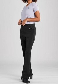 Svarta utsvängda byxor med elastisk midja och liten logodetalj, parat med en ljuslila kortärmad skjorta, bärs med svarta klackstövlar.