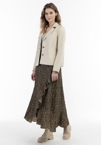 Beige getailleerde blazer met twee zilveren knopen, gecombineerd met een bruine bloemenrok met ruffles tot aan de enkel, en beige veterschoenen.