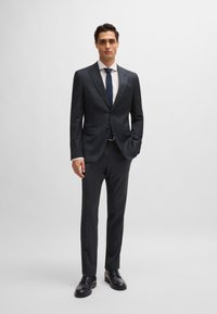 Navy suit with a single-breasted jacket and flat front trousers. White shirt underneath, paired with a matching tie and black leather shoes.