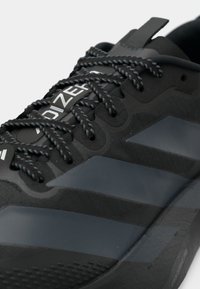 Tênis atlético preto com parte superior texturizada, detalhes cinzentos e atacadores com padrão. Apresenta um logótipo perto da língua e um design de sola flexível.