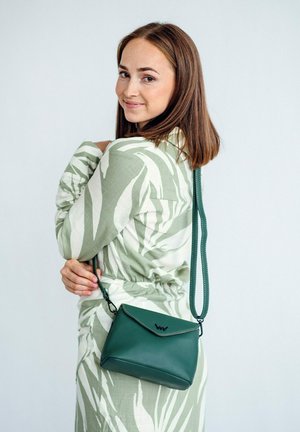 Grüne Lederhandtasche in Form eines Umschlags, mit einem Klappverschluss und einem langen, flexiblen Tragegurt. Dezente Nähte betonen das Design.