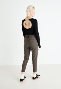 Body lungo nero con maniche lunghe e schiena scoperta, abbinato a pantaloni marroni a sigaretta e scarpe da ginnastica nere con dettagli bianchi e calzini alla caviglia.