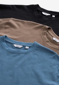 Trei pulovere cu guler rotund, bine pliate, în negru, maro și albastru, fiecare cu o etichetă vizibilă a brandului "NEXT".