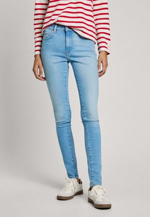 Světle modré skinny džíny z denimu, s módním pasem a čistým designem. Nosené s pruhovaným červenobílým topem a bílými teniskami.