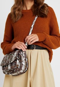 Maglione a maglia marrone, gonna beige, cintura nera. La borsa a tracolla presenta una stampa serpente nei colori marrone, bianco e arancione con una tracolla a contrasto.