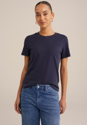 Tricou din bumbac de culoare bleumarin cu guler clasic rotund și mâneci scurte, asortat cu blugi din denim de culoare albastru deschis. Design simplu fără modele.