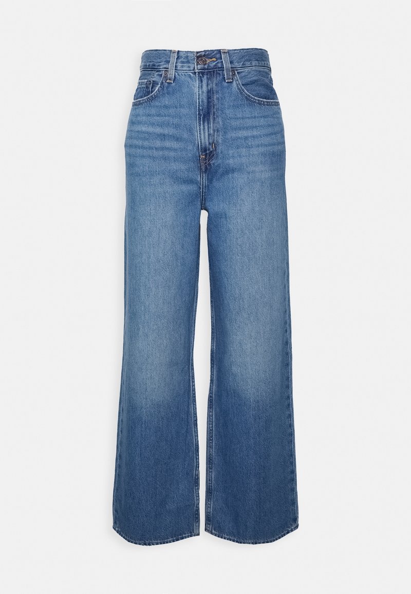 Jean en denim bleu taille haute avec jambes larges, fermeture avant par boutons et fermeture éclair, et poches avant et arrière, présenté sur un fond uni.