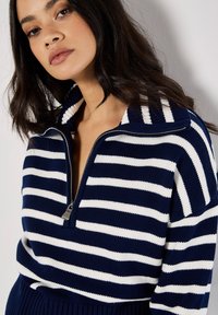 Navyblauer und weiß gestreifter Pullover mit einem Viertel-Reißverschlusskragen, gerippter Textur und kontrastierender Streifenverzierung am Kragen.